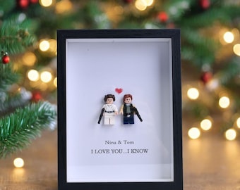 May include: A framed art piece featuring Lego figures of a couple, with a red heart above them. The frame is black, and the background is white. The text reads "Nina & Tom" and "I LOVE YOU...I KNOW".