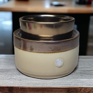 May include: A two-tiered ceramic wax warmer with a brown and beige glaze. The top tier is a metallic gold color. The warmer has a white light switch on the side.
