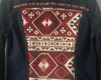 May include: A dark blue denim jacket with a colorful patterned fabric panel on the back. The panel features geometric designs in red, white, and brown.