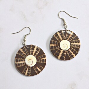 May include: A pair of brown and white shell earrings with a spiral design. The earrings are made of natural materials and have a rustic look.