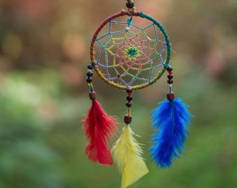May include: A colorful dreamcatcher with red, yellow, and blue feathers hanging from a tree branch.