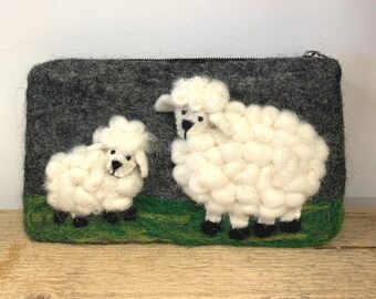 May include: A gray felt zippered pouch featuring a 3D design of a sheep and a lamb on a green grassy area. The sheep and lamb are white with black accents. The pouch is on a wooden surface.