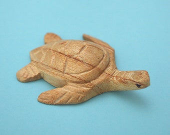 May include: Two wooden turtle figurines on a light blue background. The turtles are carved in detail and have a natural wood finish.