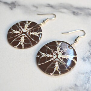 May include: A pair of brown and white patterned earrings with silver hooks. The earrings are round and have a swirling pattern.