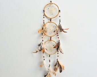 May include: A triple dream catcher with brown and white feathers hanging from three woven hoops with brown beads. The hoops are decorated with small colorful beads.