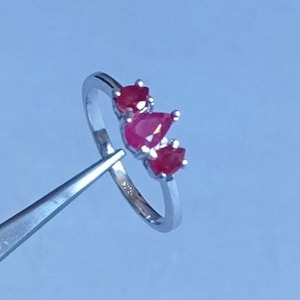 Könnte beinhalten: Ein silberner Ring mit drei roten, birnenförmigen Edelsteinen.