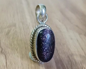 May include: A silver pendant with a dark purple oval-shaped gemstone. The gemstone has a sparkly, glittery texture.