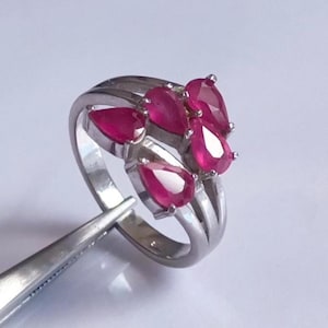 May include: A silver ring featuring five pear-shaped ruby gemstones set in a cluster design.