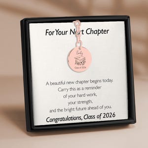 May include: A rose gold graduation charm with the name "Emily" and "Class of 2026" engraved on it. The charm hangs from a chain and is displayed in a black box with a white card that has text that reads "For Your Next Chapter".