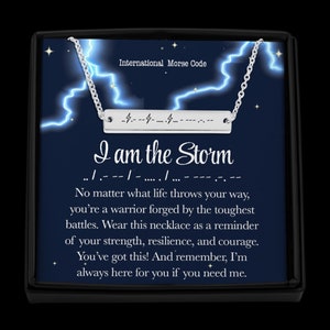 Könnte beinhalten: Eine silberne Halskette mit einem Barrenanhänger, auf dem in Morsecode "Ich bin der Sturm" steht. Die Halskette befindet sich in einer schwarzen Schachtel mit blauem Hintergrund und weißen Blitzen. Der Text unter dem Anhänger lautet: "Egal, was das Leben dir entgegenwirft, du bist ein Krieger, der in den härtesten Schlachten geschmiedet wurde. Trage diese Halskette als Erinnerung an deine Stärke, Widerstandsfähigkeit und deinen Mut. Du schaffst das! Und denk daran, ich bin immer für dich da, wenn du mich brauchst."
