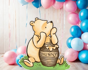 Puede incluir: Un recorte de personaje de Winnie de Pooh con un tarro de miel que dice "Hunny". El recorte está delante de un fondo de globos rosas y azules.