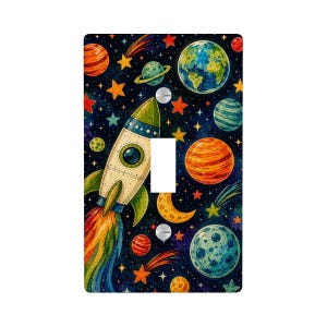 May include: A rectangular light switch cover plate featuring a colorful space-themed illustration. The design includes a rocket ship with a rainbow exhaust trail, various planets, a crescent moon, and numerous stars against a dark blue background.