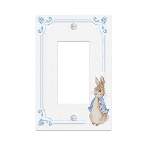 May include: White single light switch cover with a light blue border and a watercolor illustration of Peter Rabbit. The switch plate has a rectangular opening and two screw holes. The Peter Rabbit illustration is on the right side.