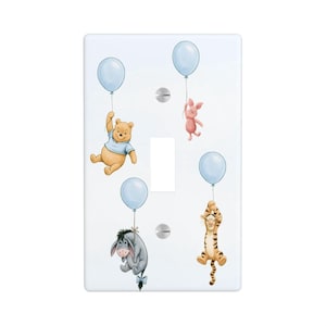 May include: A rectangular white light switch cover plate featuring a printed illustration of Winnie the Pooh, Piglet, Eeyore, and Tigger, each holding onto a light blue balloon. The plate includes two silver screws and a central toggle switch cutout.