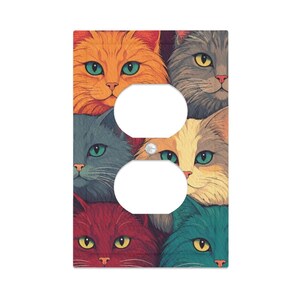 May include: A rectangular light switch wall plate cover featuring a colorful illustration of multiple cat faces in shades of orange, gray, yellow, red, and teal. The plate has two circular cutouts for a duplex outlet and a central screw hole.