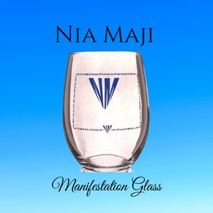 May include: A clear glass with a white label that says "NIA MAJI" and a blue logo. The text "Manifestation Glass" is written in cursive below the glass.