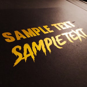 Puede incluir: Un fondo negro con las palabras "SAMPLE TEXT" en letras doradas. La palabra "SAMPLE" está en una fuente estilizada y dentada.