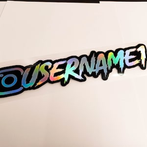 May include: A holographic sticker with a black background and a white Instagram logo and the text "USERNAME" in a stylized font.