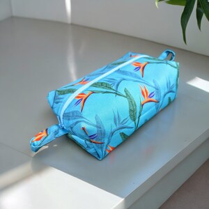 May include: A blue zippered pouch with a tropical bird of paradise print. The pouch has a zipper closure and a carrying handle.