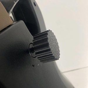 May include: Close-up of a black guitar featuring a textured, ridged knob. The knob is attached to the guitar's body, which has a smooth, matte finish. The guitar's strap is visible.