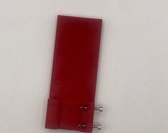 May include: A red plastic part with two silver screws. The part has a rectangular shape with a small rectangular extension on the bottom.