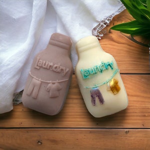 May include: Two brown and white soap bottles shaped like milk jugs with the word "Laundry" embossed on them. Each bottle has a string of clothes hanging from it.