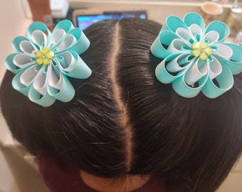 May include: Two light blue and white ribbon hair bows with green centers. The bows are tied together with a clear elastic band.