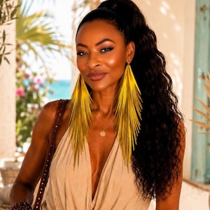 May include: A pair of long, pointed, bright yellow statement earrings with a textured, fan-like design. The earrings feature a sharp, multi-layered fringe structure that hangs vertically, creating a bold, elongated silhouette against the face.