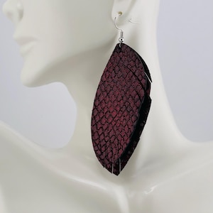 May include: A pair of large, layered earrings with a burgundy snakeskin pattern. The earrings are suspended from silver-colored fish hook ear wires. The earrings are displayed on a white mannequin head.