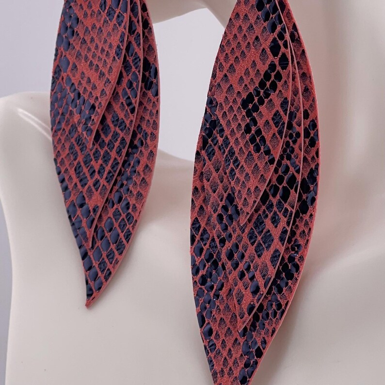 Peut inclure: Une paire de grandes boucles d'oreilles superpos&eacute;es avec un motif peau de serpent. Les boucles d'oreilles sont de couleur corail avec un motif bleu marine fonc&eacute;. Les boucles d'oreilles sont en forme de feuilles et sont pr&eacute;sent&eacute;es sur un mannequin blanc.