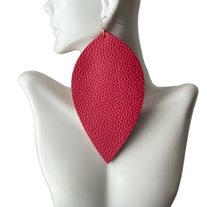 May include: A pair of large, red leather earrings shaped like a teardrop. The earrings are made of a textured leather and have a gold hook.