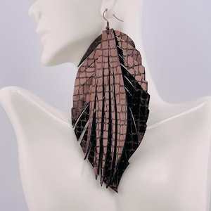 May include: Large, brown and black faux leather feather earrings. The earrings have a textured, crocodile-like pattern and are designed to dangle. The earrings are shown on a white mannequin bust.