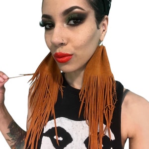 May include: A pair of long, brown leather fringe earrings. The earrings are made of suede and have a tassel design.