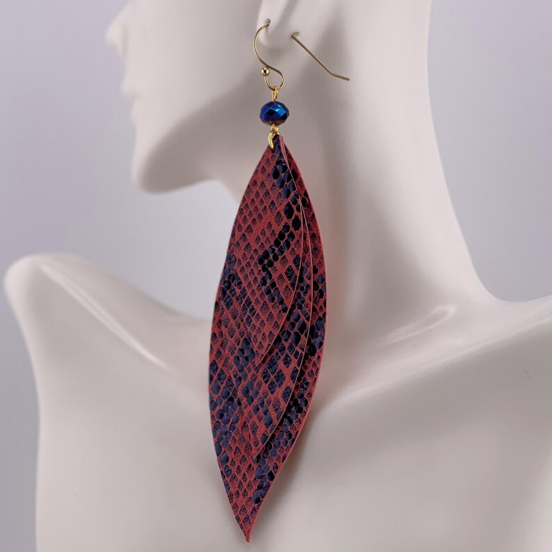 Peut inclure: Une paire de longues boucles d'oreilles superpos&eacute;es avec un motif peau de serpent rouge et bleu marine. Les boucles d'oreilles sont suspendues &agrave; des crochets dor&eacute;s et comportent une petite perle bleu fonc&eacute; en haut.