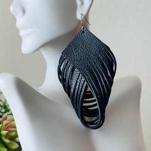 May include: Black leather fringe earrings with a geometric shape. The earrings are long and dangle from the earlobe.