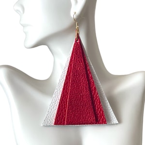 May include: A pair of large triangle-shaped earrings made of layered leather. The top layer is white, the middle layer is red, and the bottom layer is white. The earrings are hanging from gold hooks.