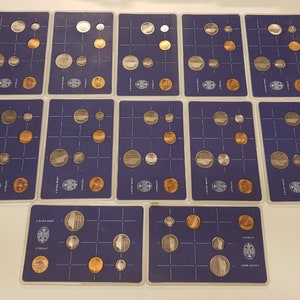 May include: A collection of 15 coin display cards with a blue background. Each card features a grid of 9 slots, filled with various coins. The coins are arranged in a pattern, with some coins being silver and others being copper.