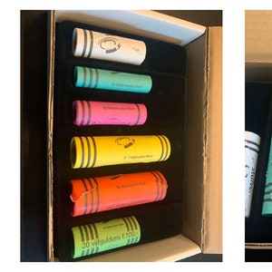 May include: A set of 10 colorful crayons in a cardboard box. The crayons are arranged in a row and are labeled with their colors. The colors include red, orange, yellow, green, blue, purple, pink, brown, black, and white.