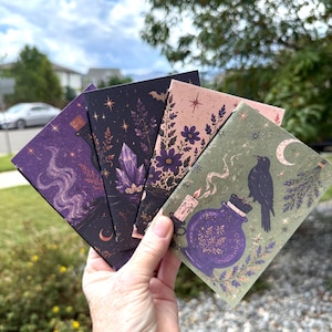 May include: Four rectangular cards featuring dark, illustrated designs. The cards display motifs of purple potion bottles, glowing crystals, floral patterns, a lit candle, and a black bird perched on a bottle, all accented with stars and moons.