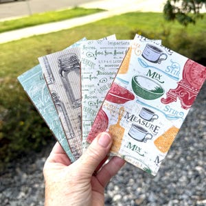 May include: Four rectangular cards featuring kitchen-themed designs. One card displays colorful illustrations of bowls, cups, and spoons with the text "MIX," "STIR," and "MEASURE." Others show vintage-style spice labels, glass jars, and script typography.