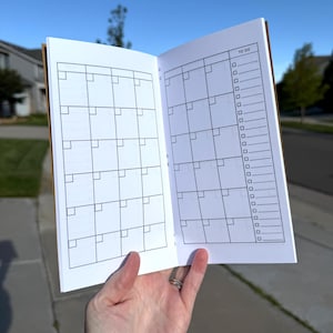 May include: An open planner with white pages featuring a black printed monthly calendar grid on the left side and a matching calendar grid alongside a vertical to-do list with checkboxes on the right side, labeled with the text TO DO at the top.