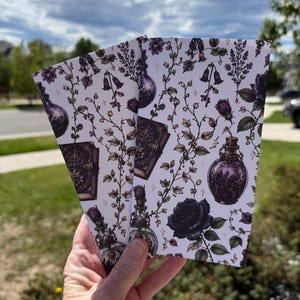 May include: Two rectangular bookmarks featuring a white background with a repeating pattern of dark purple potion bottles, ornate vintage books, black roses, and delicate climbing vines with small bell-shaped flowers and tiny four-pointed stars.