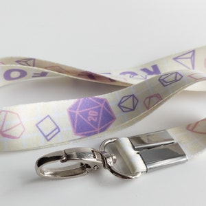 May include: A white lanyard with a purple and pink dice pattern and the text "Roll for it" printed on it. The lanyard has a silver swivel clip.