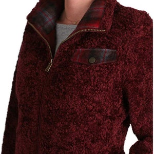 May include: A burgundy sherpa jacket with a plaid lining and a zipper closure. The jacket has a flap pocket on the chest with a button closure.
