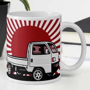 Może przedstawiać: Biały ceramiczny kubek z grafiką białej ciężarówki i czerwonym wzorem wschodu słońca. Ciężarówka ma czarne koła i czarny kontur. Kubek ma biały uchwyt i jest na białym tle.
