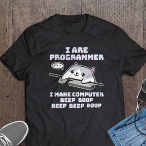 Op de afbeelding: Zwart T-shirt met een witte cartoonkat die op een keyboard speelt. De tekst op het shirt luidt "I are programmer I make computer beep boop beep beep boop".