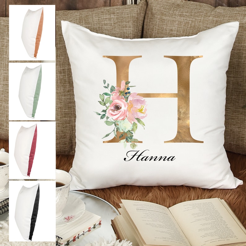 May include: White pillow with a gold letter H and pink floral design. The name Hanna is written below the letter.