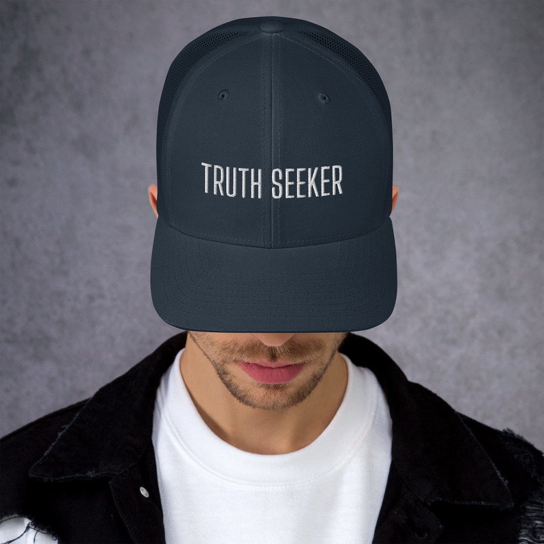 May include: A navy blue mesh trucker hat with a white embroidered design that says "TRUTH SEEKER".