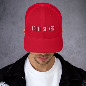 May include: A red and black mesh trucker hat with the text "TRUTH SEEKER" embroidered in white on the front.