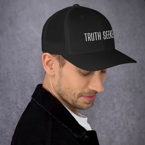 May include: A black mesh trucker hat with a black front panel and white embroidered text that reads "TRUTH SEEKER".